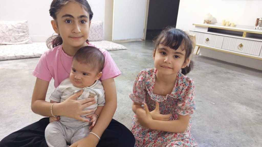 Baby Nazar held by one of his sisters, with another sister sitting beside them.