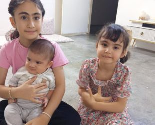 Baby Nazar held by one of his sisters, with another sister sitting beside them.